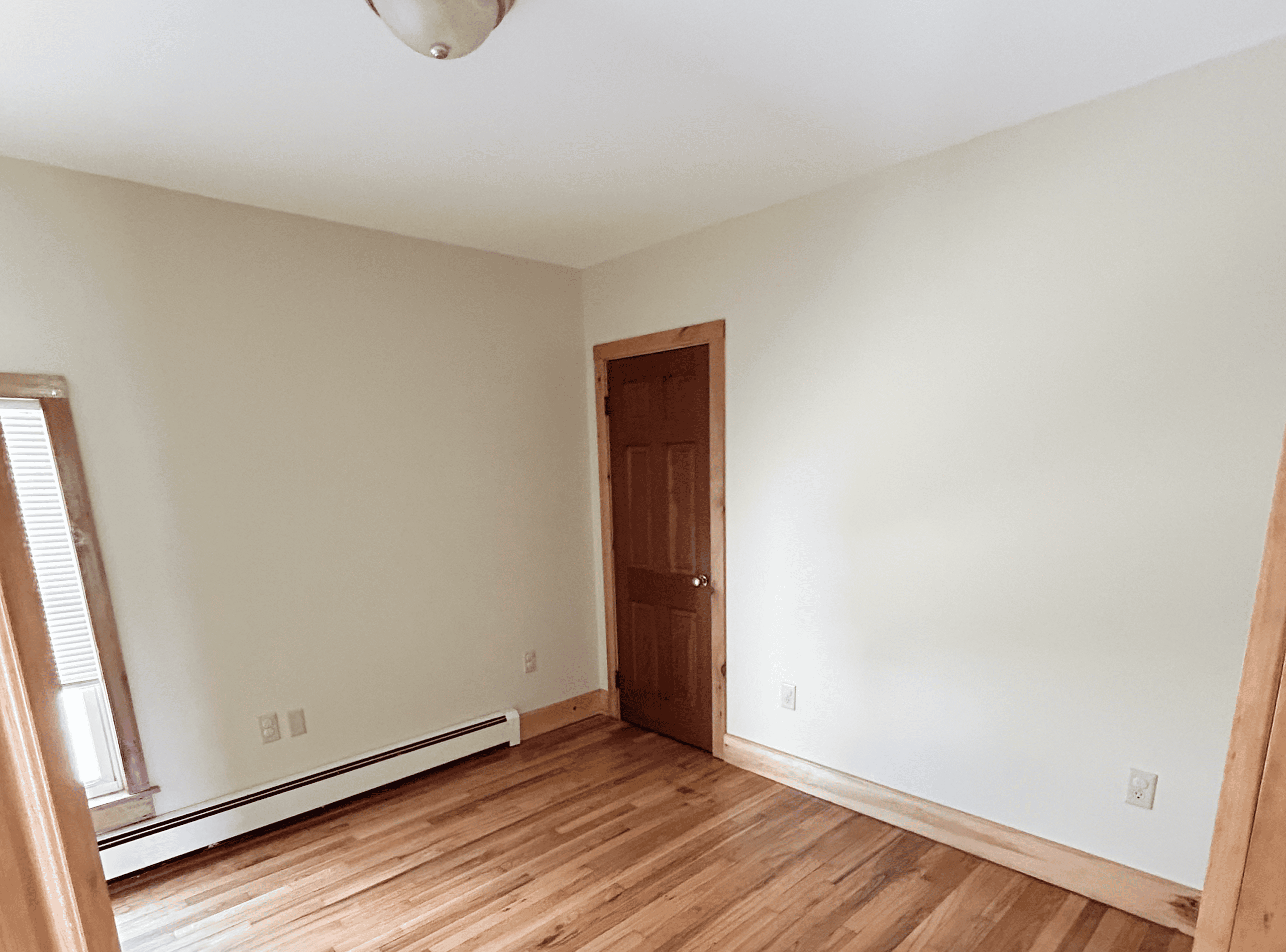 Living Room Interior with Hardwood Floors Spacious living room with hardwood flooring, neutral wall colors, and a wooden door, ideal for home.